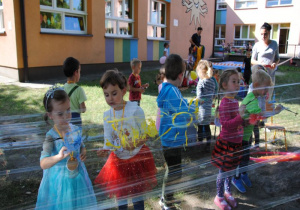 dzieci malują farbami na folii zawieszonej między drzewami w ogrodzie pod opieką nauczycielki